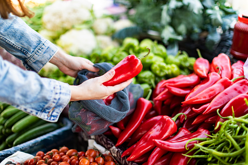 Young adult woman buying red bell pepper at market with reusable bag