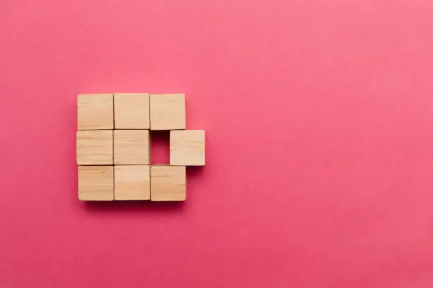 Nine small wooden block cubes are building one big cube on pink background. One of the cubes is about to leave the big cube. Standing out from the crowd concept.