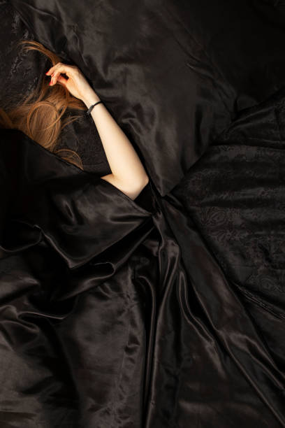 Female red hair and a hand on black bed sheet.