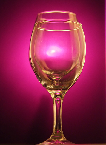 A pair of wine glasses in front of a purple background.
