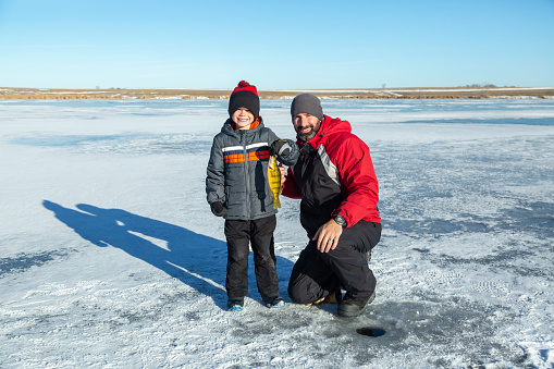 Father & son holding up the perch the young boy just caught while ice fishing on a winter day.