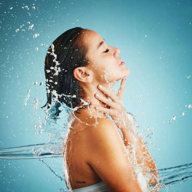 istock Water, hydration and cleansing with a woman in studio on a blue background with a liquid splash for hygiene. Relax, luxury and wellness with an attractive young female washing in a bathroom or shower 1455812428