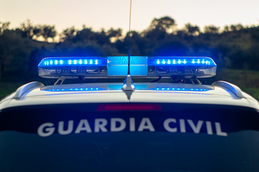 Fotografía al atardecer de un coche de la guardia civil con el puente de señales encendido.