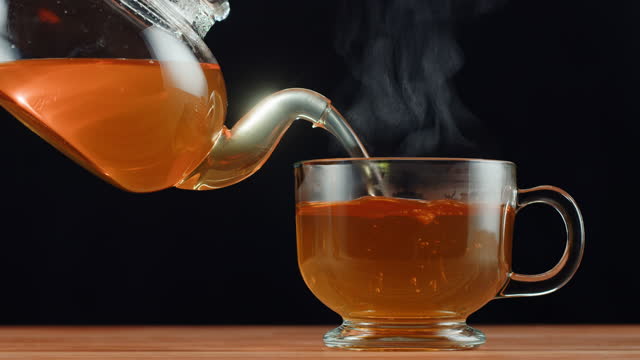 Pouring citrus black tea on black background. Freshly brewed green tea ceremony process, healthy morning, detox drink.
