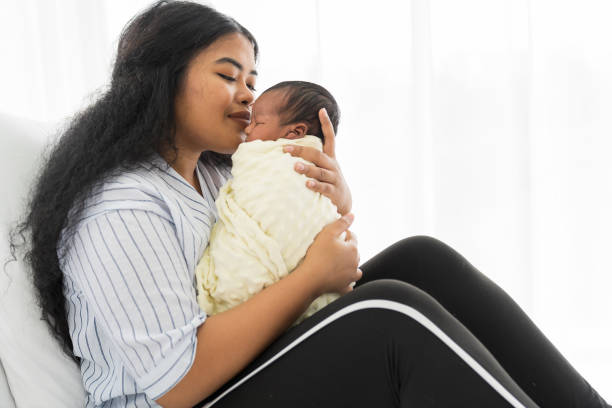 happy mother carrying and kissing on newborn baby on bed. young mom or nurse taking care newborn in the hospital - mother baby new kissing imagens e fotografias de stock