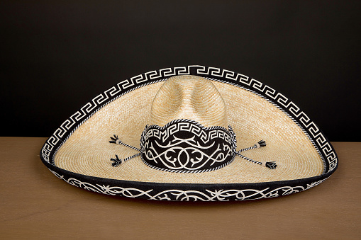 HANDCRAFTED COWBOY AND CHARRO HAT WOVEN BY HAND WITH PALM MADE IN MEXICO WITH MATERIALS. ON WOODEN TABLE AND BLACK BACKGROUND