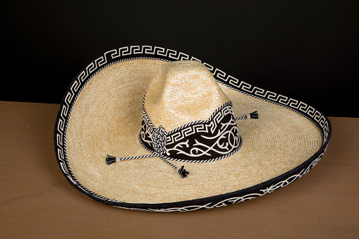 HANDCRAFTED COWBOY AND CHARRO HAT WOVEN BY HAND WITH PALM MADE IN MEXICO WITH MATERIALS. ON WOODEN TABLE AND BLACK BACKGROUND
