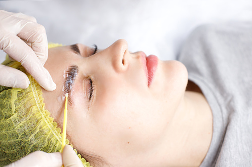 beautician applying composition for eyelash lamination to woman close-up