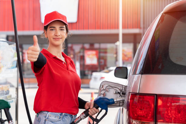 attendant service female worker refuelling car at gas station. assistant woman worker wear red uniform and red hat refuelling car at petrol station - gas station fuel pump station gasoline imagens e fotografias de stock