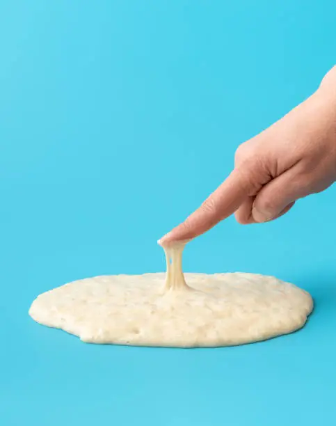 Woman is testing the sourdough yeast with one finger, minimalist on a blue table.