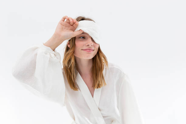 pretty young woman in silk fabric white nightgown and sleep mask looking at camera. - one woman only young women people nightie imagens e fotografias de stock