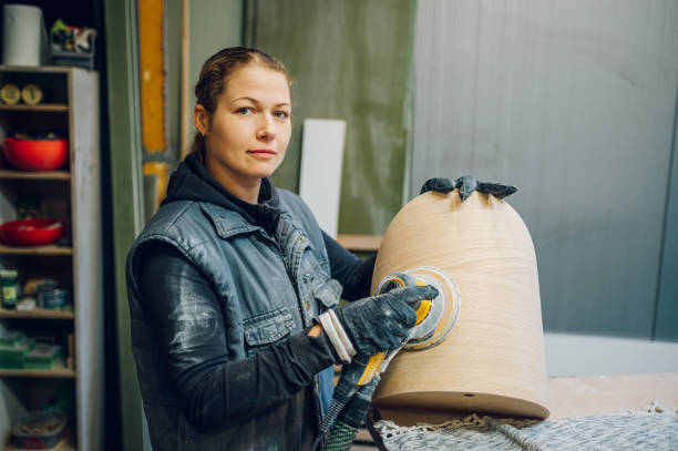 istock Blonde female carpenter using an electric sander in a workshop or factory 1455836508