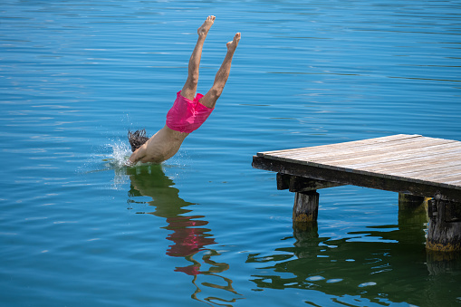 Young Hispanic man head jumping into the lake from wooden pier at summertime.