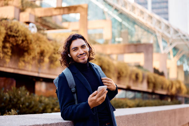 istock Young happy Hispanic entrepreneur using cell phone outdoors and looking at camera. 1455853259