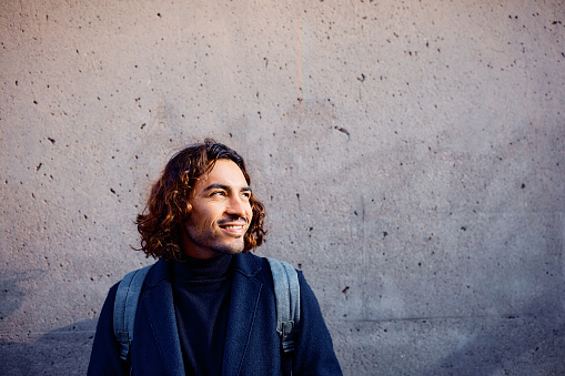 Young smiling Hispanic entrepreneur standing against the wall and looking away. Copy space.