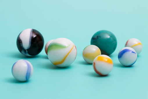 Toy marbles in a variety of colors arranged on an aqua colored background. Shallow depth of field.