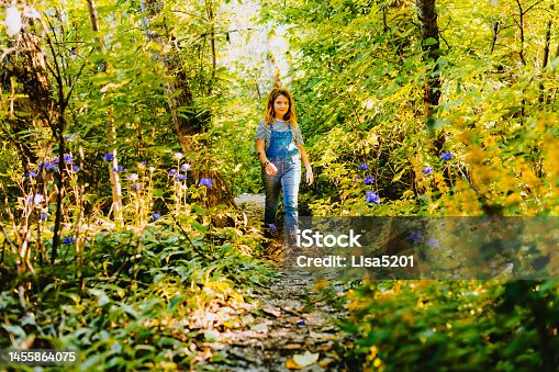 istock Girl walks through a forest full of lush wildflowers and wild grasses on a beautiful sunny day in nature 1455864075