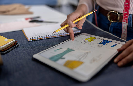 Close-up on a fashion designer sketching dresses at her atelier and using a tablet computer