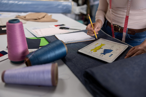 Close-up on a fashion designer working at her atelier sketching a design while looking at fabrics and threads