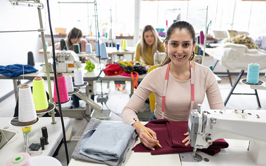 Latin American seamstress working at a clothing atelier sewing clothes on a machine - people at work concepts