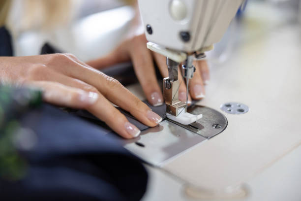 Close-up on a seamstress sewing clothes at an atelier on a machine - small business concepts