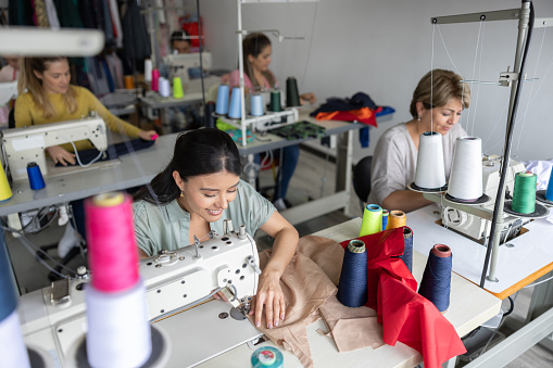 Group of workers sewing clothes at an atelier using sewing machines - small business concepts