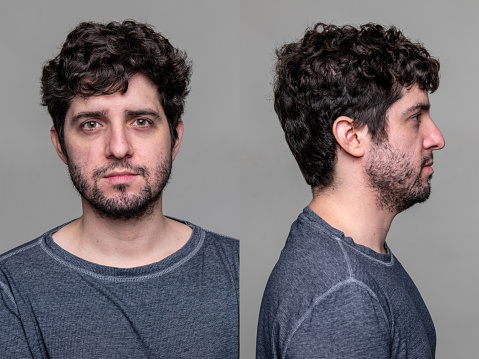 Profile portrait of middle-aged bearded man in white t-shirt over grey studio background, copy space. Side view of handsome confident man posing on gray, standing straight and looking aside