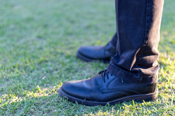 Black shoes of man standing on a grass field during sunset