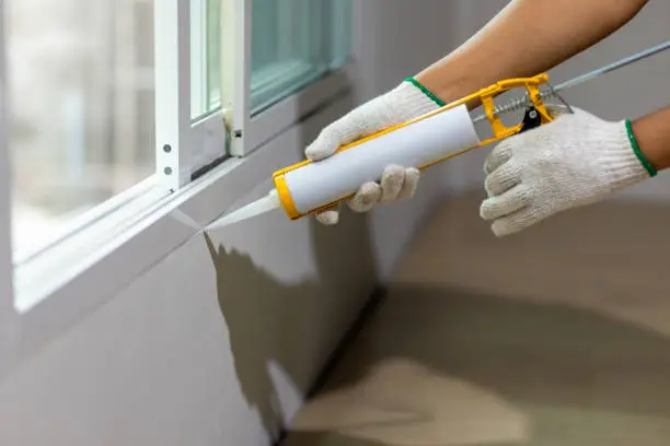 Photo of Construction worker using silicone sealant caulk the outside window frame.