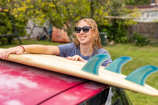 Teenage Girl Loading a Surfboard onto a Car