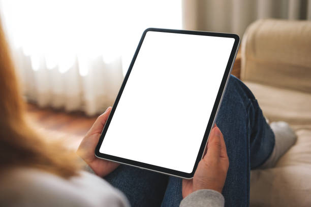 istock Mockup image of a woman holding digital tablet with blank desktop screen while lying on a sofa at home 1455873360