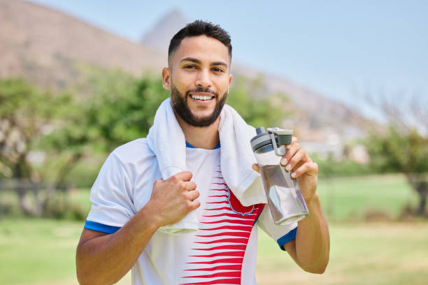 porträt-, fitness- und fußballspieler-trinkwasser im training, cardio-training und fußballfeld-workout. glücklicher, sportlicher und gesunder mann, der sich entspannt und eine ruhepause mit einem flüssigen getränk genießt - soccer player soccer men smiling stock-fotos und bilder