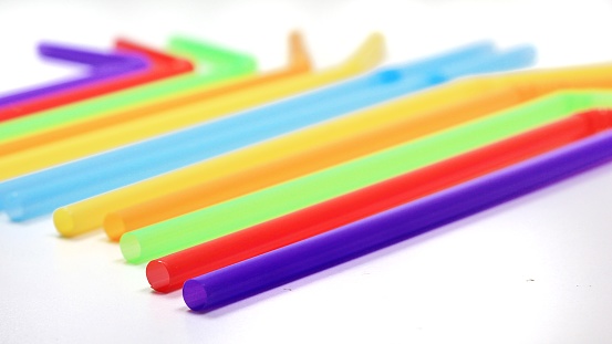 Blue, yellow, orange, green, red and blue drinking straws are placed on a white background. Take a photo from below