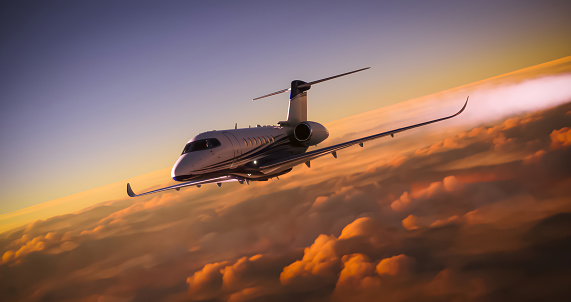 A luxury private jet overflying cloudy skies at sunset