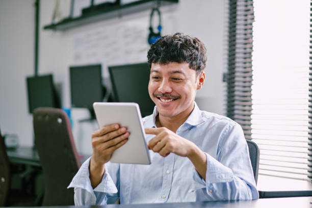 istock Smiling young asian businessman touching digital tablet and checking online information in the modern office 1455896093