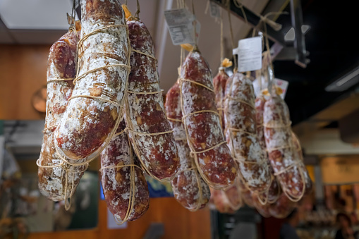 Salami sausage on display for sale hanging at a salumeria meat and cheese shop in Central Market Mercato Centrale in Florence, Italy