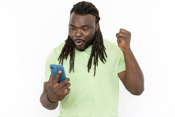 istock Black man celebrating victory while looking at phone screen 1455899035