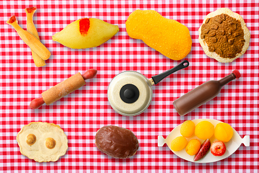 Overhead shot of old miniature toy cooking utensils and food on gingham check tablecloth.