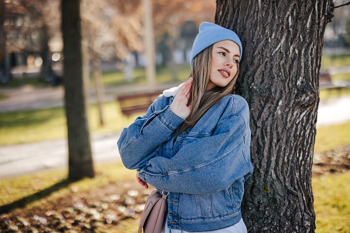 Beautiful young woman leaning on tree and posing in city park