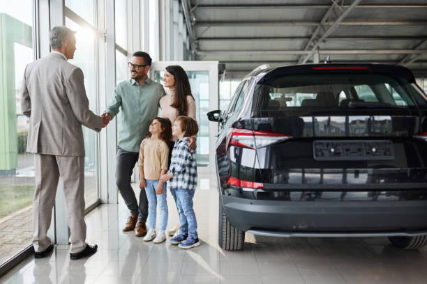 familia joven y feliz estrechando la mano de un vendedor de automóviles en una sala de exposición. - new automobile fotografías e imágenes de stock