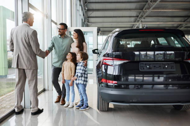 młoda, szczęśliwa rodzina ściskająca dłoń sprzedawcy samochodów w salonie. - new car zdjęcia i obrazy z banku zdjęć