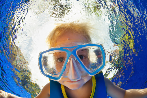 Happy little kid in snorkeling mask jump and dive underwater in coral reef sea lagoon. Family travel lifestyle in summer adventure camp. Swimming activities on beach vacation with child.