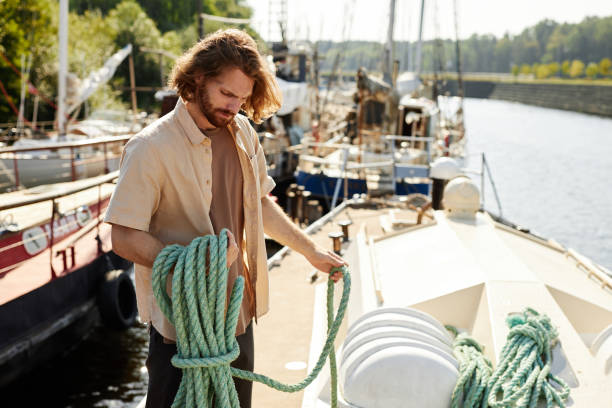 istock Handsome long haired man standing on boat in dock and holding line 1455913771