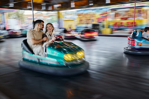 Happy couple having fun while driving bumper car at amusement park. Blurred motion. Copy space.