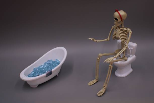 istock Skeleton wearing a red headband with a bow is sitting on a toilet getting ready to take a bath 1455914001