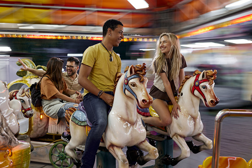 Cheerful couples having fun during carousel ride at amusement park. Blurred motion.