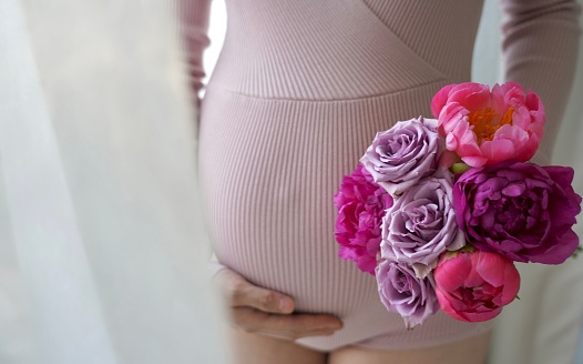 A closeup of a pregnant woman's belly holding flowers in her hand ,for photoshoot