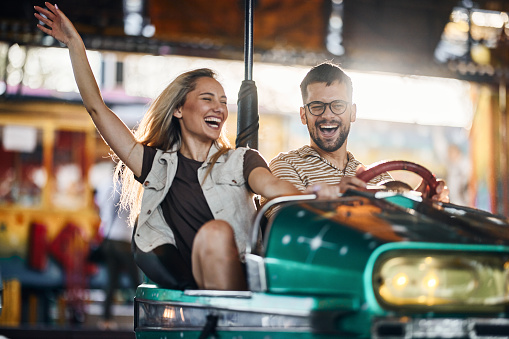 Young happy couple having fun in bumper car at amusement park.