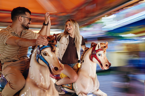 A woman and her young daughter enjoying a day out together at the fair in Newcastle upon Tyne, North East England. They are riding on different creatures on the carousel while smiling, the girl is looking at her mother.