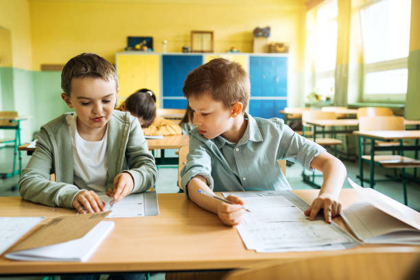 istock Elementary schoolboys writing in workbook at desk in classroom 1455915991